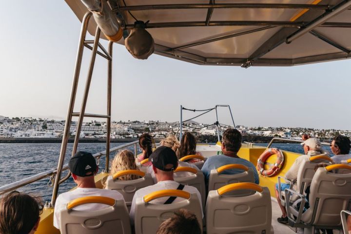 People seated on a boat, viewing a coastal town across the water.
