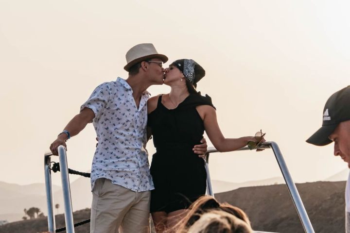 Couple kissing on a boat deck with a scenic background under a clear sky.