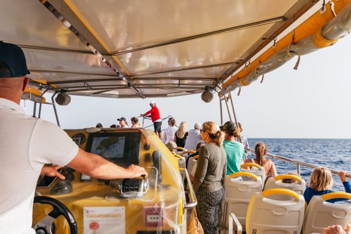 People on a covered tour boat observing the ocean, with a guide standing at the front.