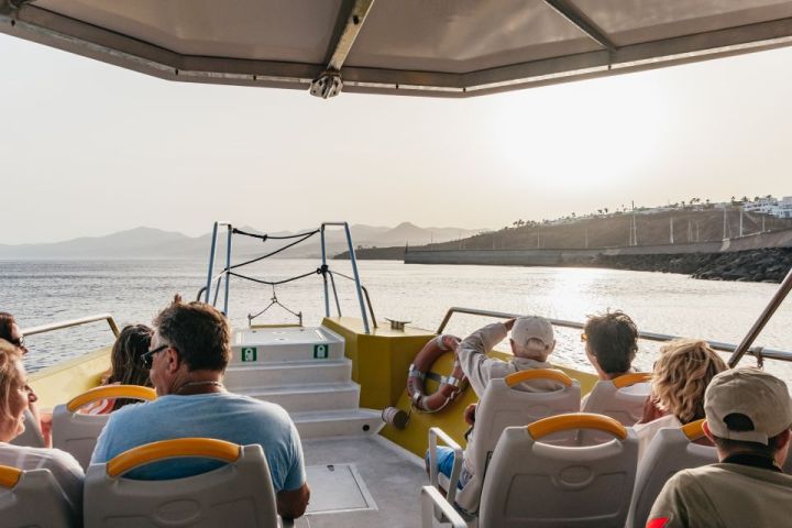 People on a boat looking at the ocean and distant coastline during sunset.