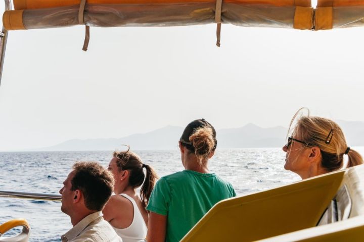 Four people on a boat looking at the sea and distant hills.