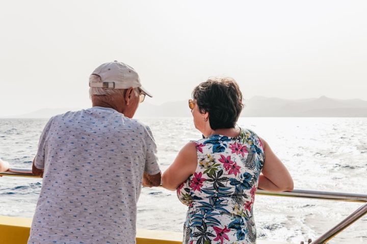 Two people leaning on a boat railing, gazing at the sea and distant mountains.