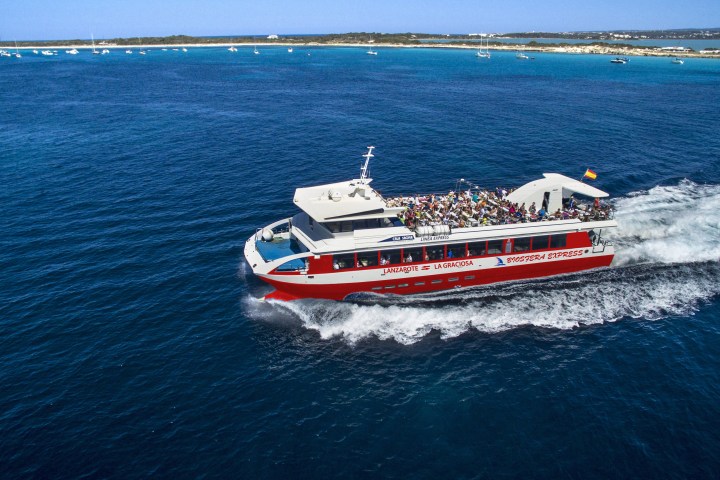 Red and white ferry boat sailing on blue ocean with people on board.