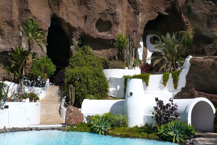 White buildings and greenery set against rocky cliffs and a turquoise pool.