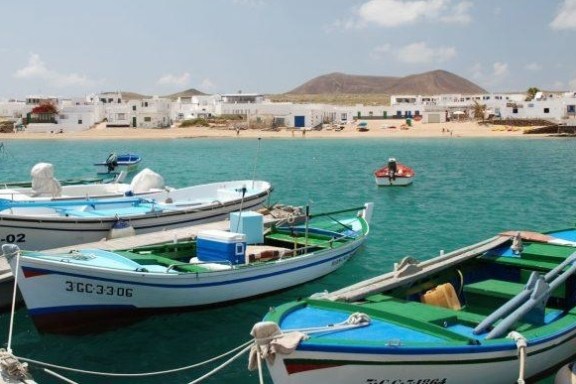 Small boats docked by a turquoise sea with sandy beach and white buildings in the background.