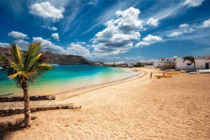 Sandy beach with palm trees, turquoise water, and blue sky with clouds.