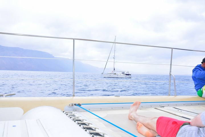People relaxing on a boat with a sailboat in the distance on the ocean.