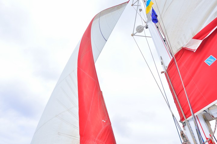Close-up of a sailboat's red and white sails against a cloudy sky.