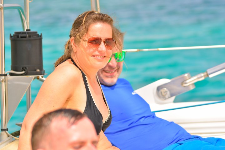 Two people relaxing on a boat in sunny weather, with turquoise water in the background.
