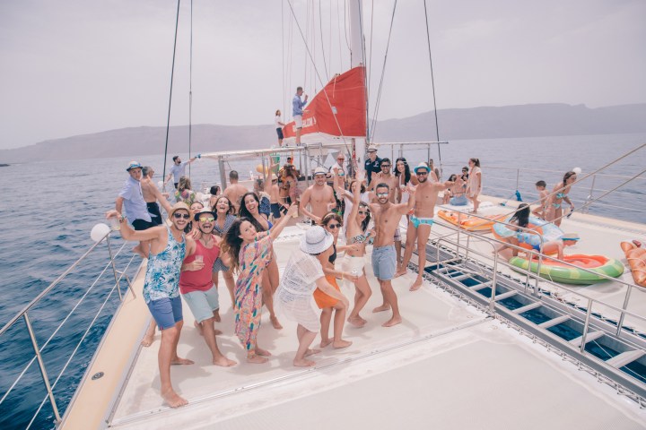 Group of people having a party on a yacht with red sails on open water.