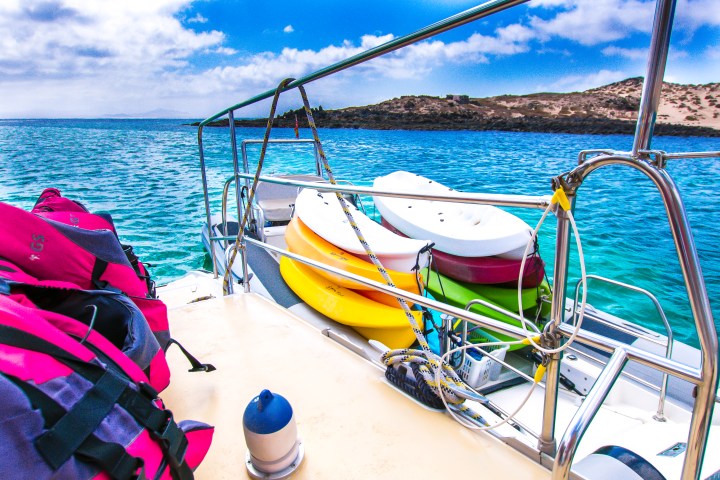 Colorful kayaks on a boat deck with life vests, near a turquoise sea and rocky shore.