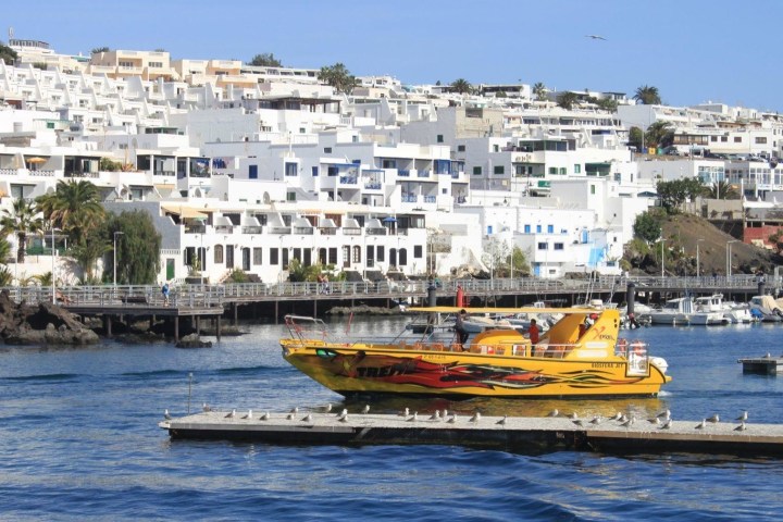 Yellow boat in harbor with white buildings in background.