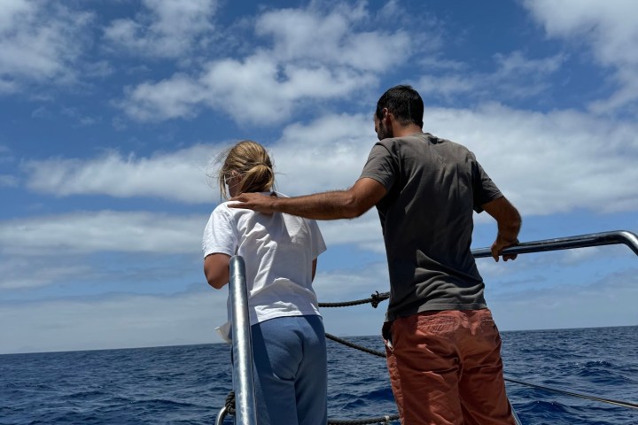 Two people stand on a boat looking at the ocean under a partly cloudy sky.
