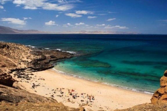 Scenic view of a sandy beach with turquoise water and rocky cliffs under a blue sky.