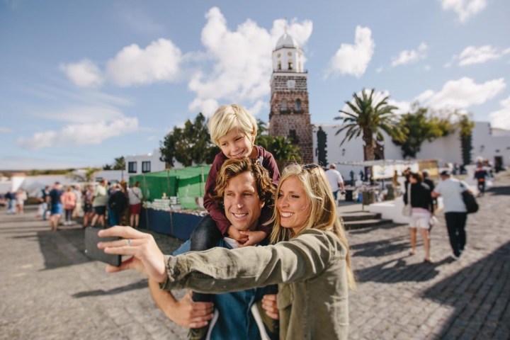 Family taking a selfie in a plaza with a church tower and palm trees in the background.