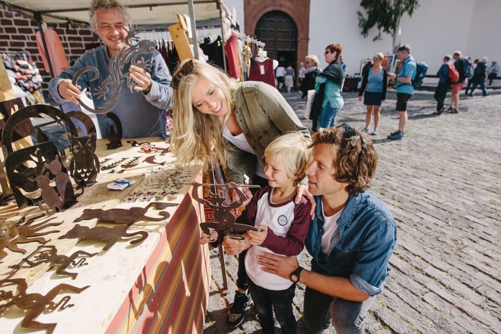 Family browsing metal art at outdoor market, vendor smiling, sunny day.