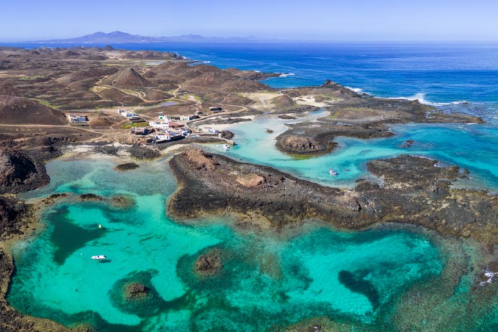 Aerial view of a rocky coastline with turquoise waters and small white buildings.