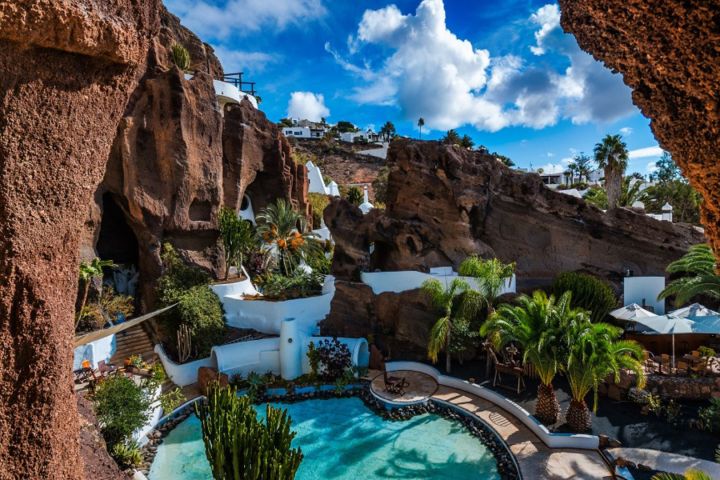 Scenic pool surrounded by rock formations and palm trees under a blue sky with clouds.
