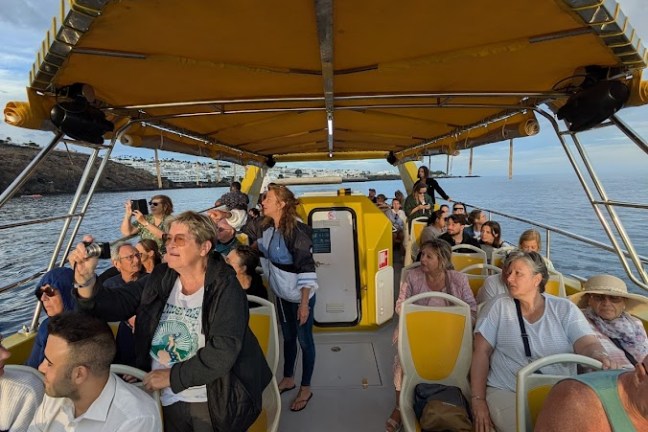 Group of people on a boat under a yellow canopy, with a scenic sky backdrop.