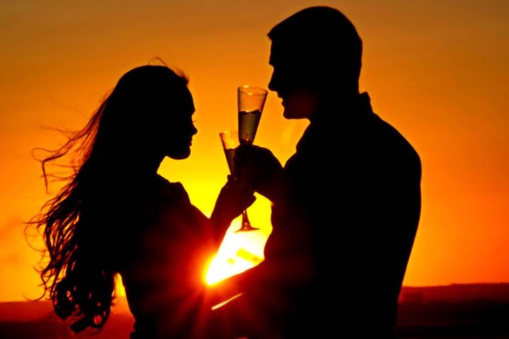 Silhouetted couple drinking champagne at sunset.