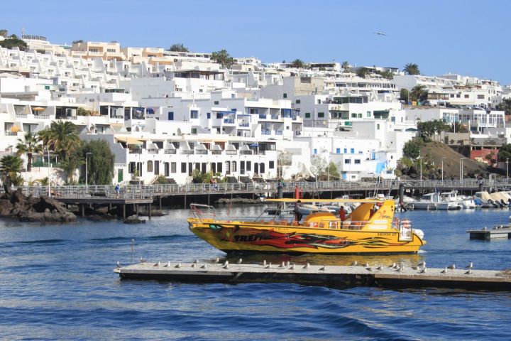 Yellow tour boat on water before hillside white buildings and greenery.